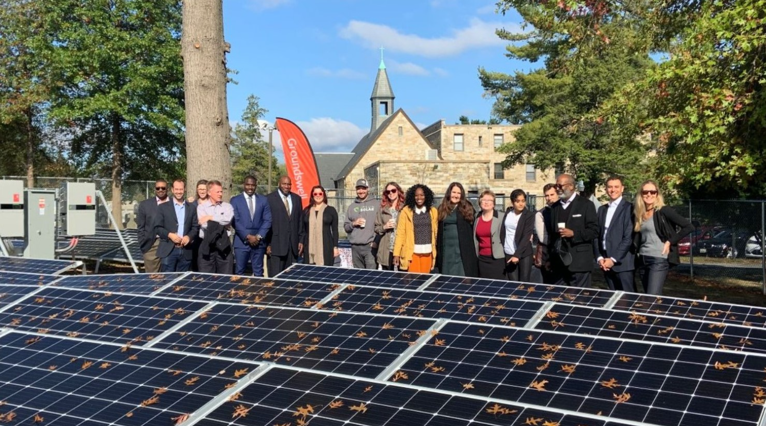 A group of people pose for a photo in front of a solar panel array.