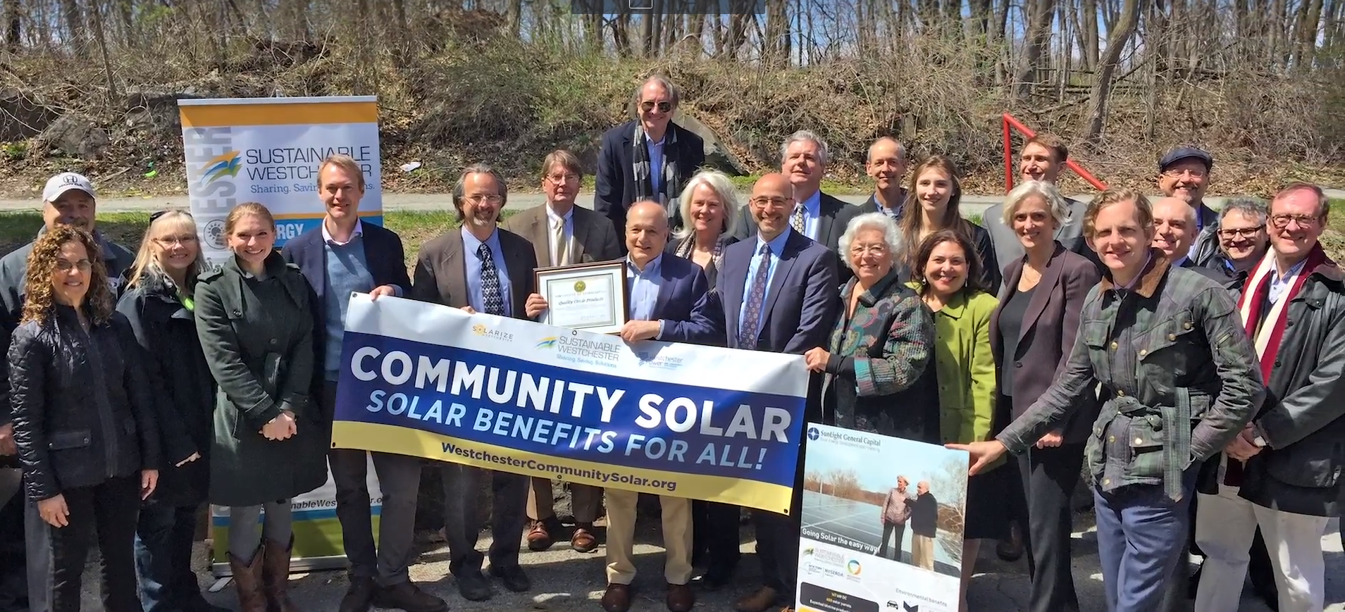 A group of people pose for a group photo with a sign that says "Community Solar Solar Benefits for All!"