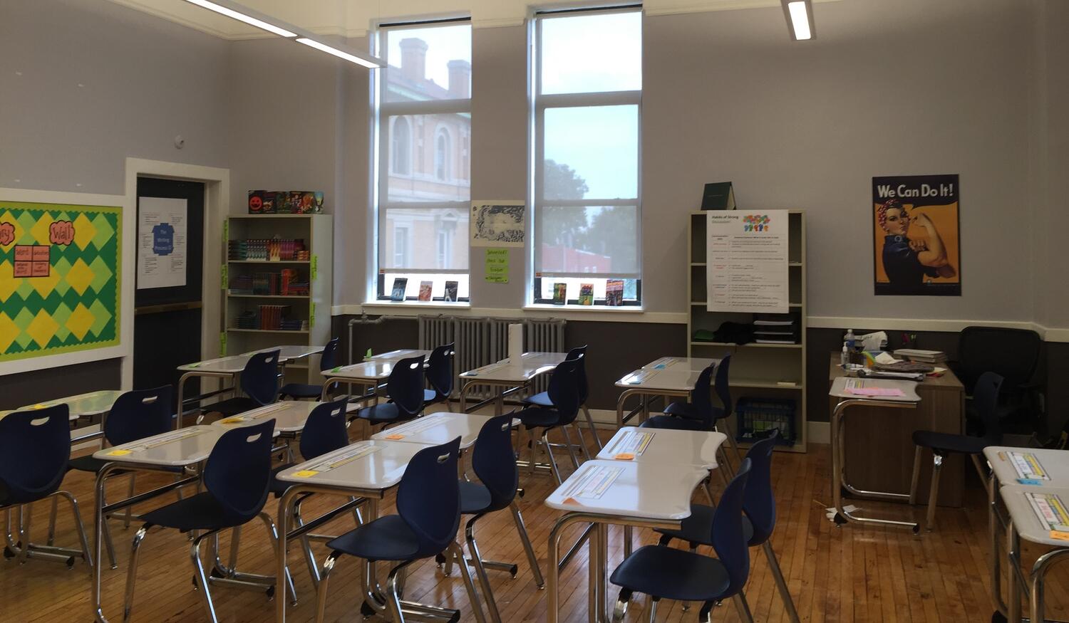 An empty school classroom with student desks left and center and a teacher's desk in the top right