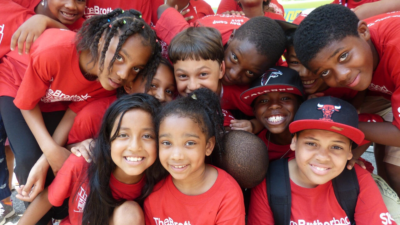 A group of young children staring directly at the camera, wearing red t-shirts. 