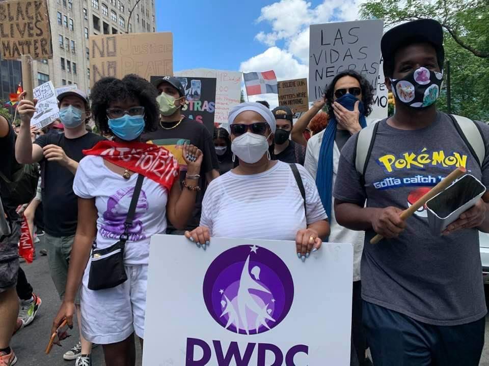 A group of masked people march in the street carrying a sign that says "DWDC"