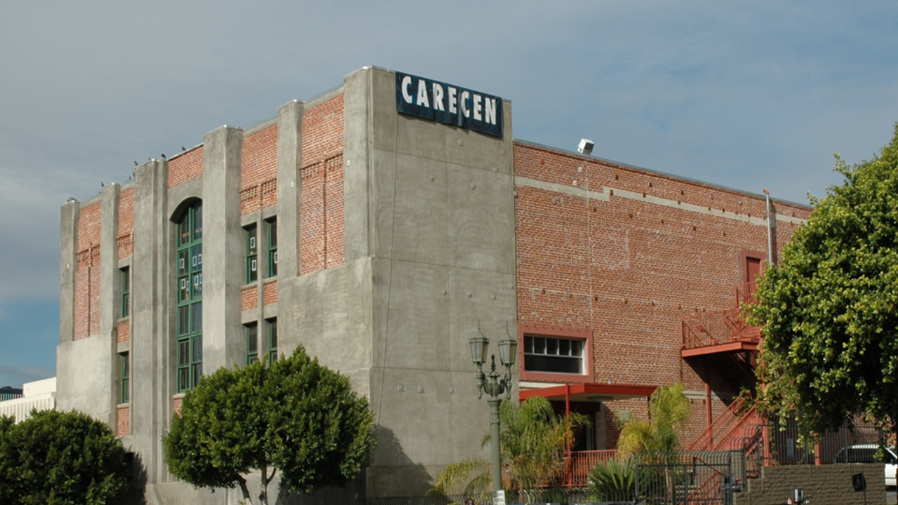 Corner of a red brick and gray cement building with CARECEN banner hanging on the top right.