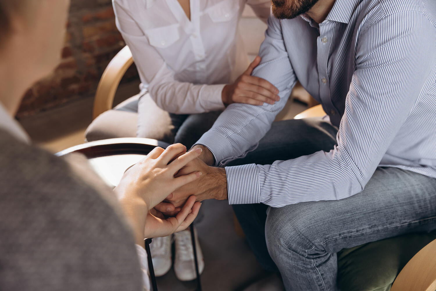 Stock image of two people comforting a third man by holding his hands and right arm.