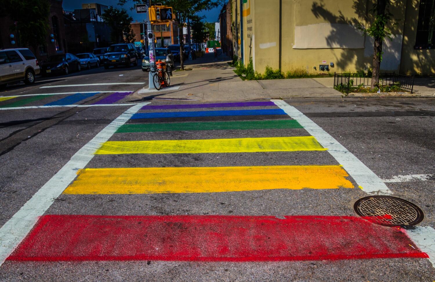 Close up of New York City street with horizontal lines moving away from the camera like a ladder. The colors appear in the following order form closest to furthest away: red, orange, yellow, green, blue, purple