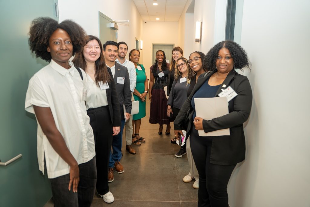People lined up along a hallway smiling toward the camera as they get ready to tour the facility.