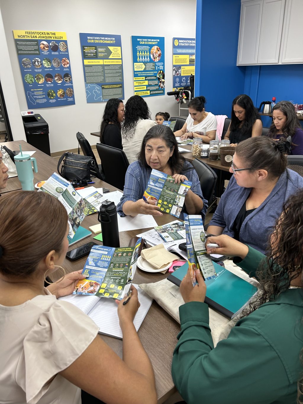 A group of women are seated at a table looking at a flyer together.