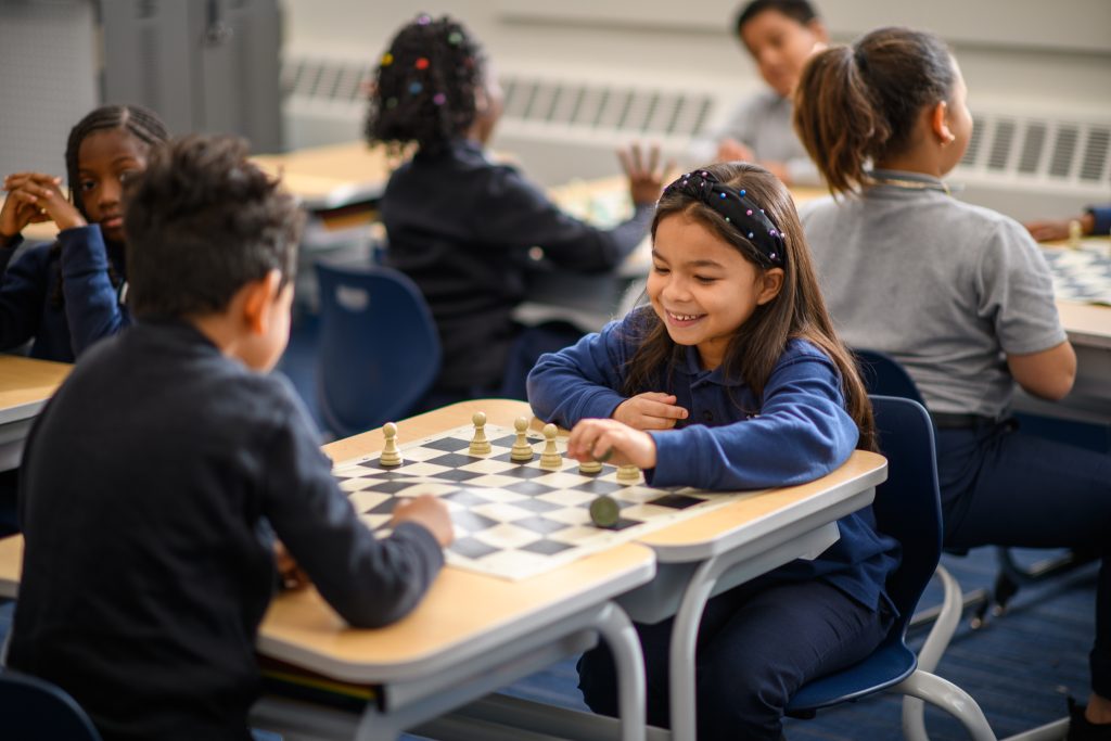 Two Bold students play a game of chess at their desks.