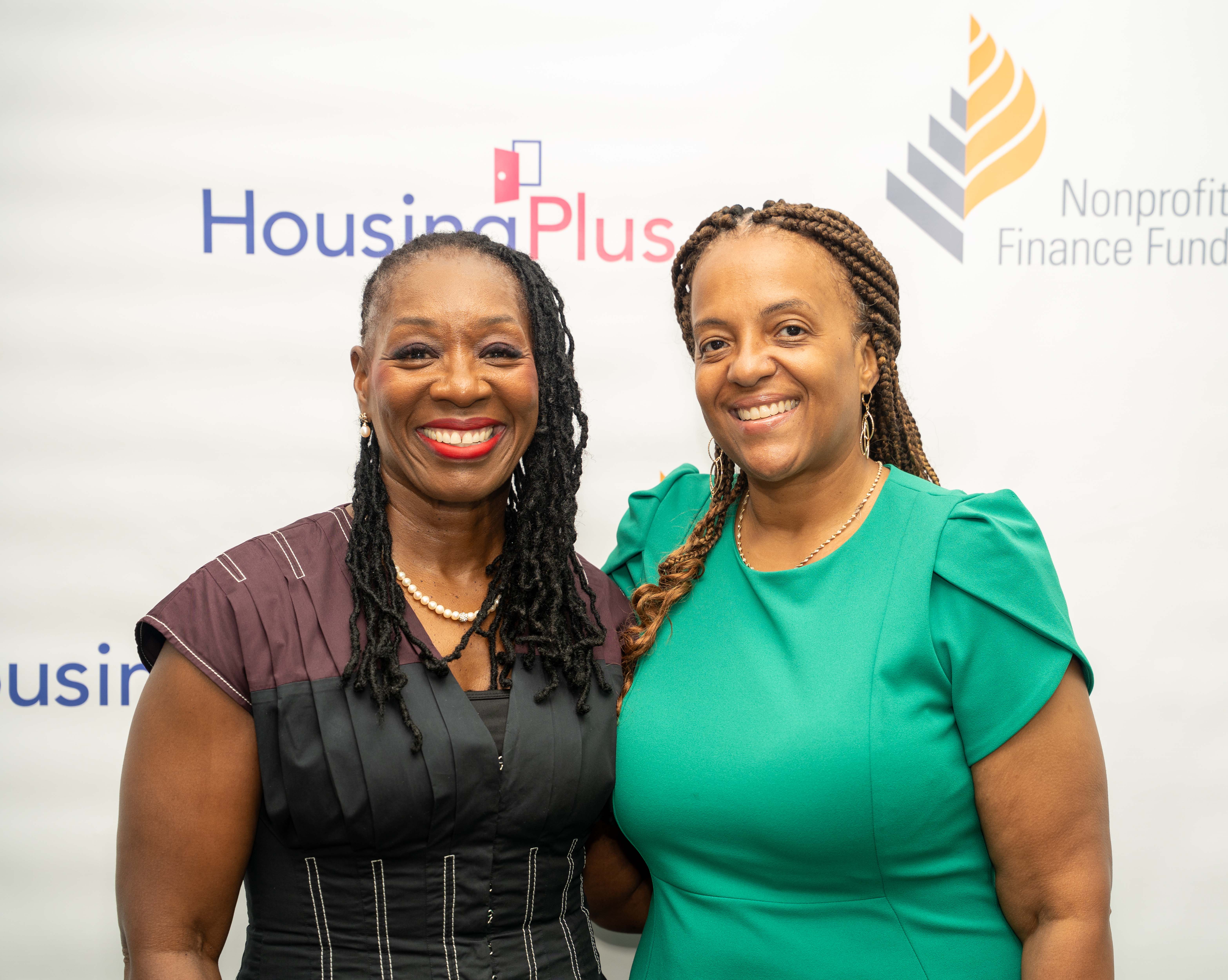 Aisha Benson and Karen Ford, CEO of HousingPlus, smiling in front of a banner with logos.