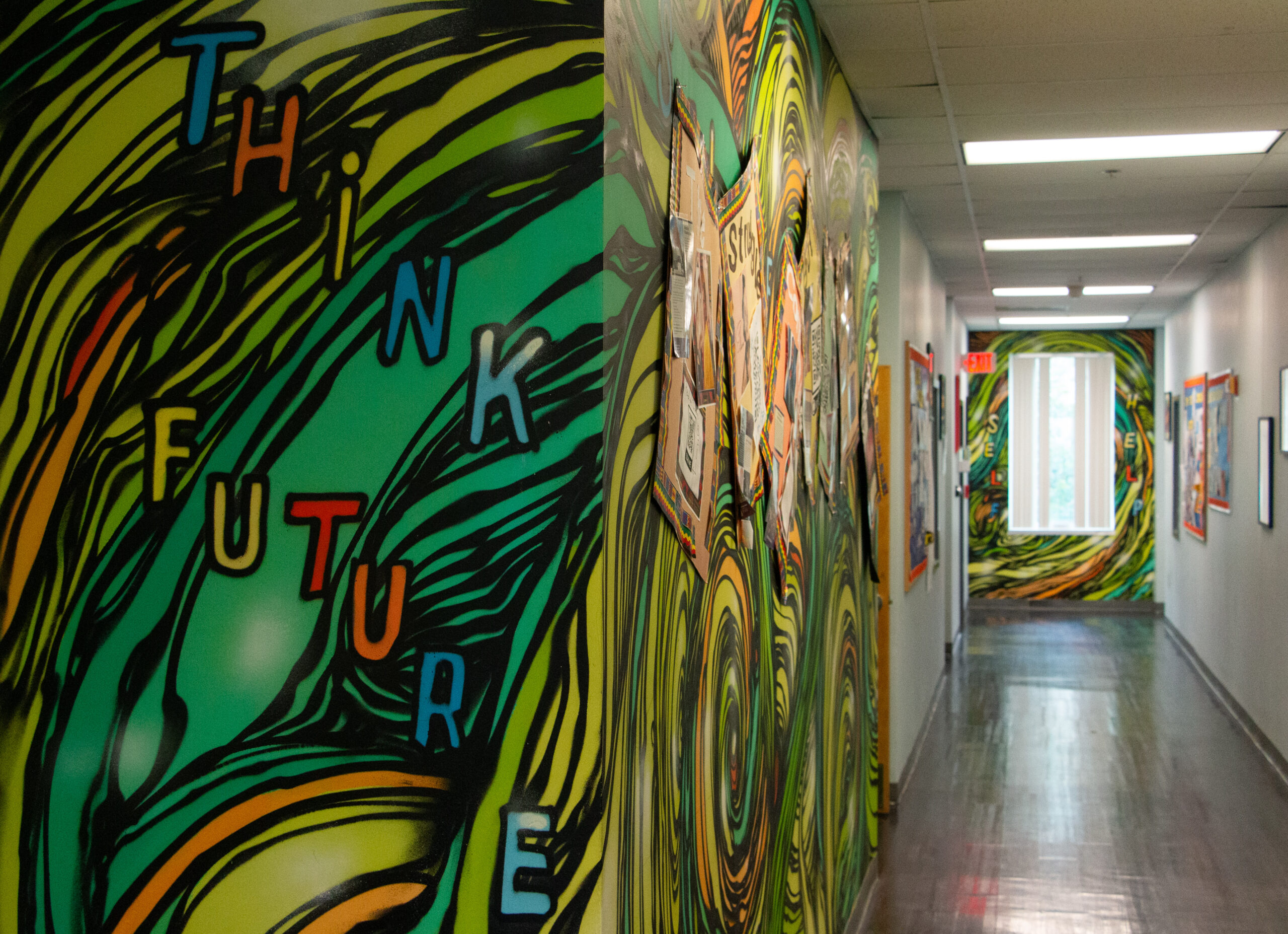 Hallway with vibrant mural art featuring swirling green and yellow patterns. The words "Think Future" are painted boldly. Bright, creative atmosphere.