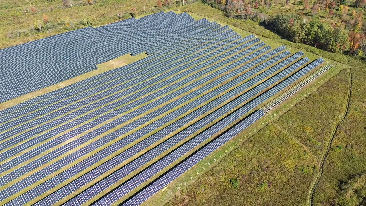 Aerial view of an expansive solar farm with rows of solar panels on green grass, surrounded by trees. The scene conveys sustainability and innovation.