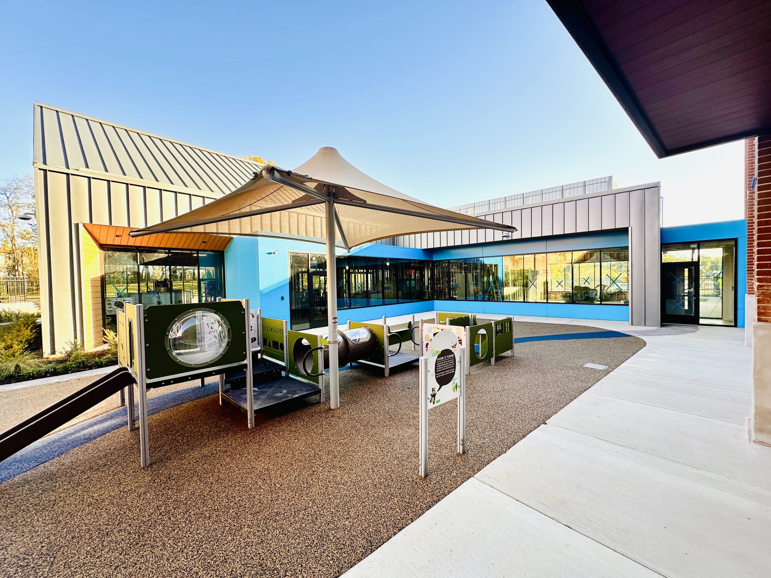 A playground with circular tubes and windows sits in the center of a courtyard for a new ECE facility.