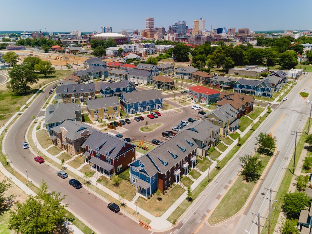 Aerial view colorful housing units in curved around a parking lot with sidewalks and cars parked around each unit.