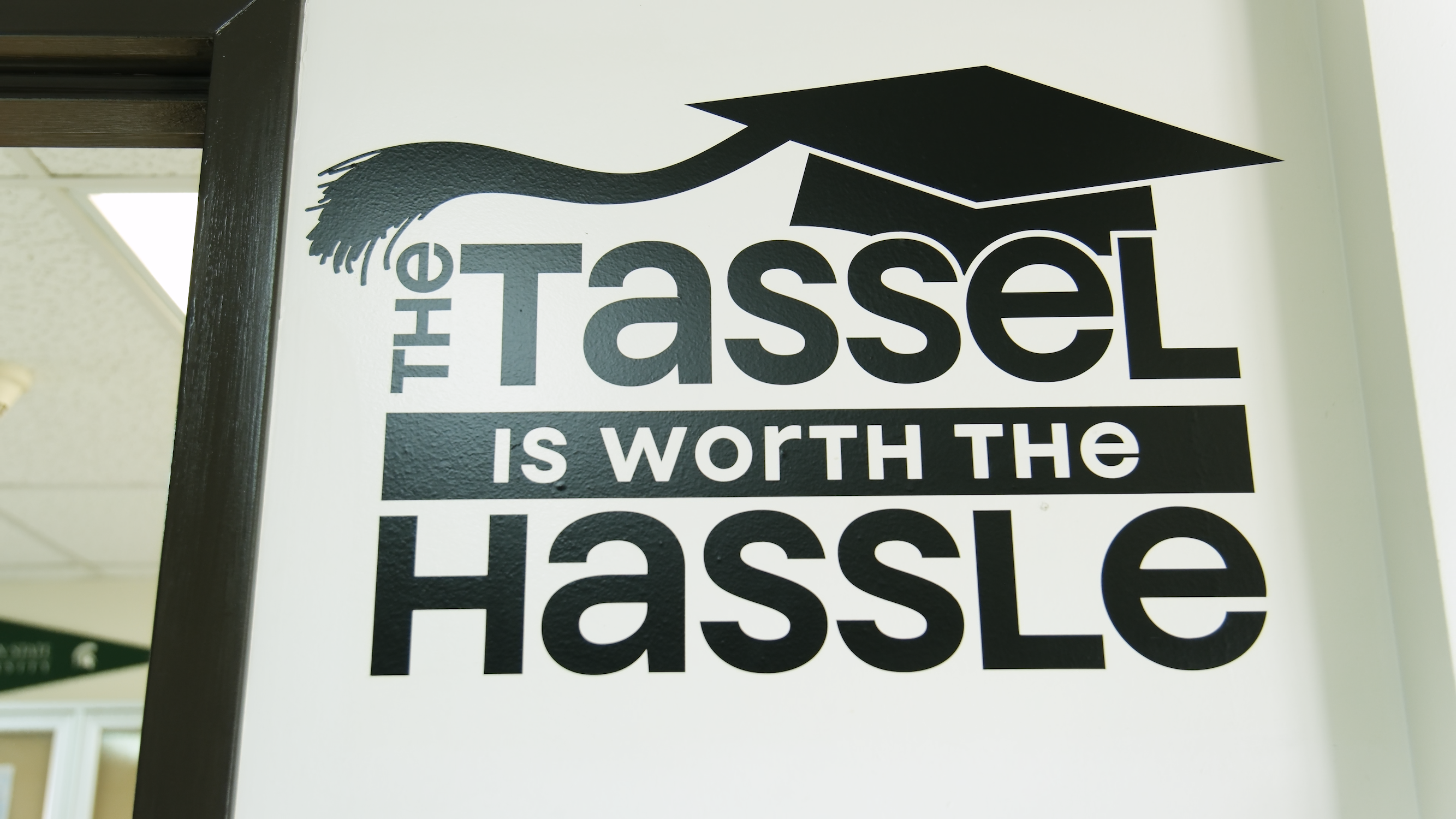 A black wall decal with a graphic of a graduation cap reads, "The Tassel is Worth the Hassle."